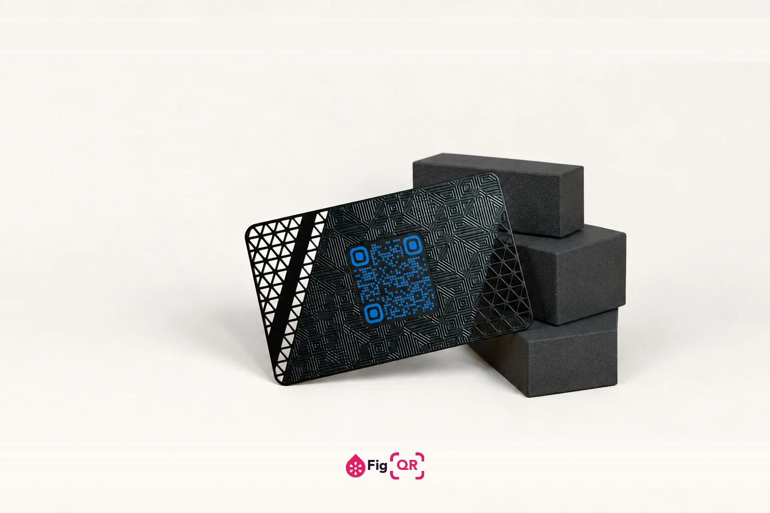 A matte black metal business card with an etched geometric pattern, propped against dark grey blocks on a plain cream background, with a blue QR code in a recessed panel at its centre.