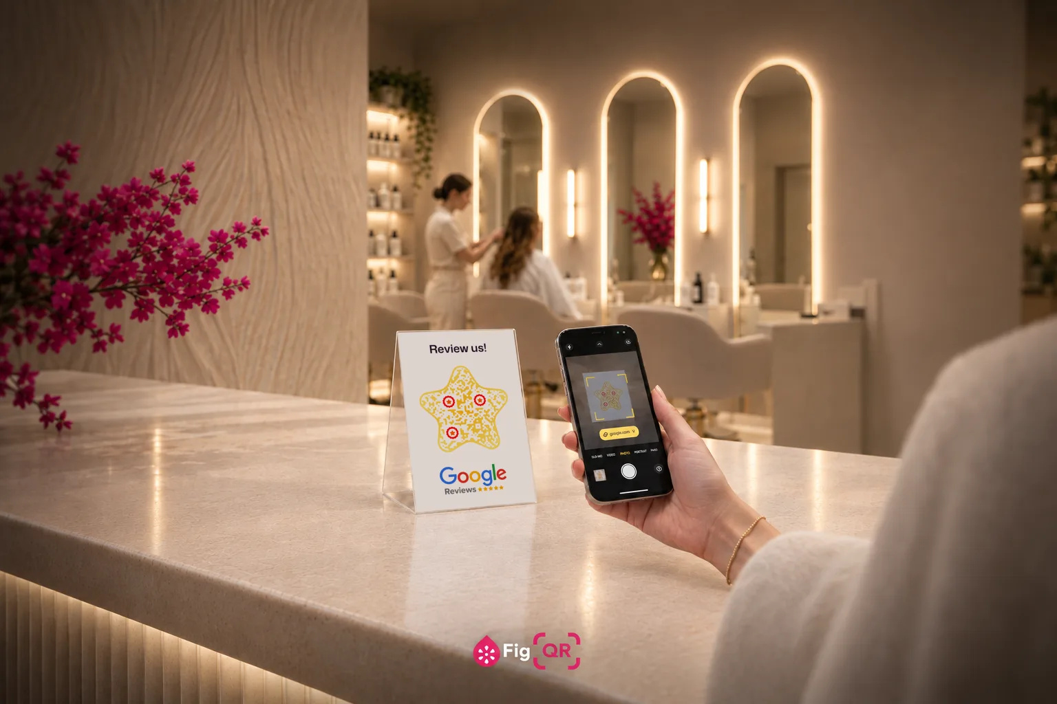 A salon reception desk in warm light. A small acrylic stand holds a card reading 'Review us!' above a gold star-shaped QR code and the Google Reviews logo, while a customer holds up a phone whose camera shows the same code.